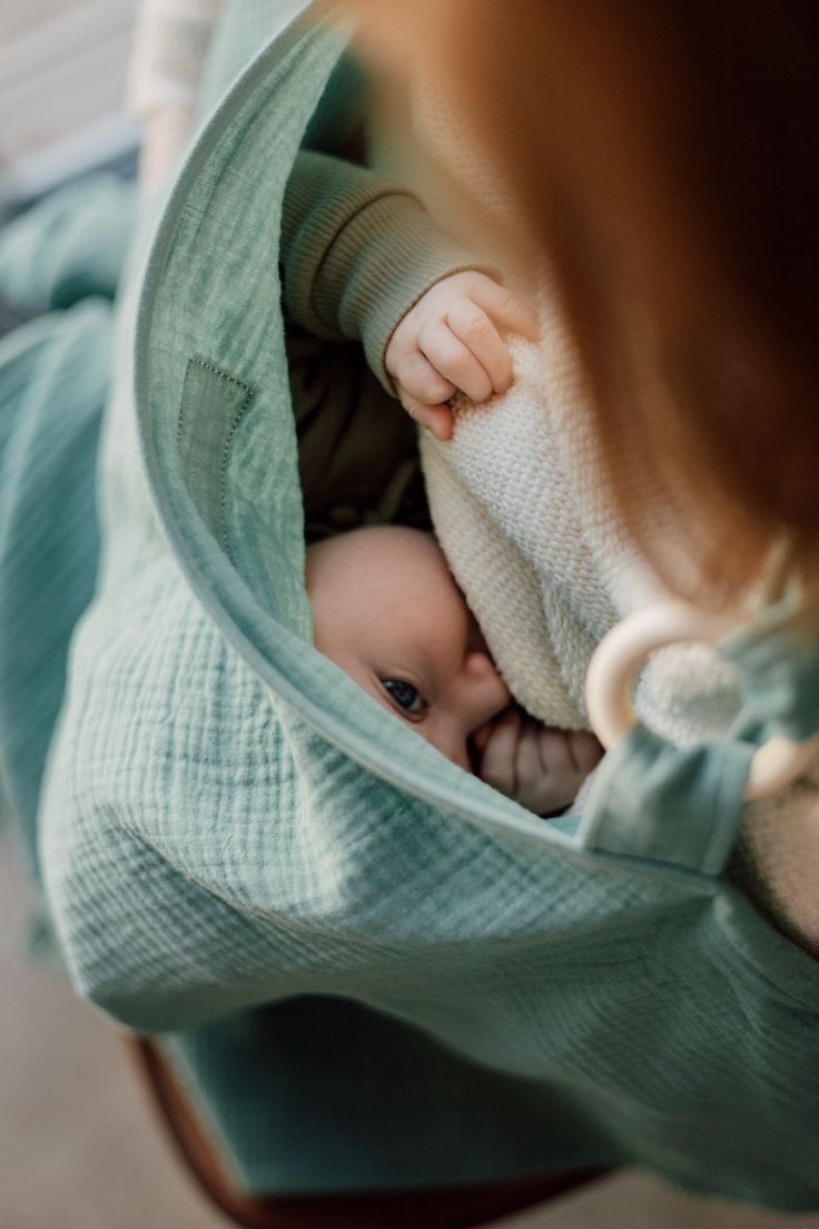 en mamma som ammar sin bebis och använder en amningsfilt